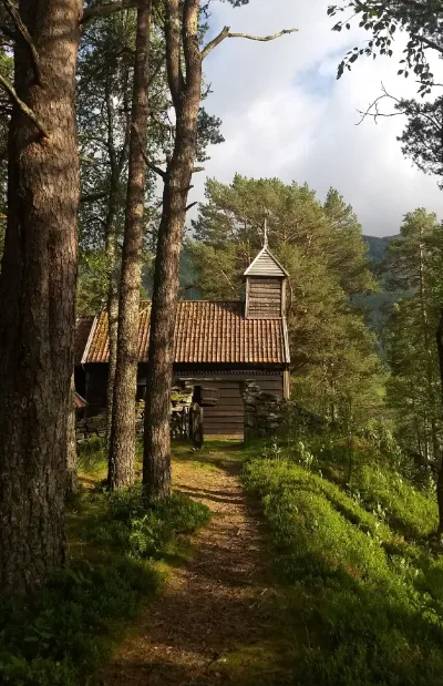 Hestad Kapell set mellom høye tre i kveldssolen